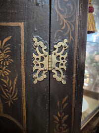 A decorative butterfly hinge on a wooden Chinese black corner cabinet.