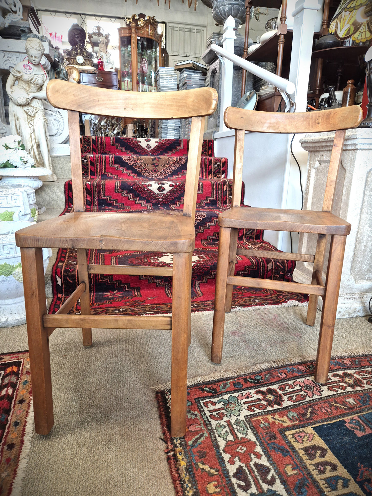 Pair of wooden childrens school chairs on a patterned rug with decorative items in the background