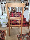 Wooden childs school chair on a patterned rug with decorative items in the background. back view.