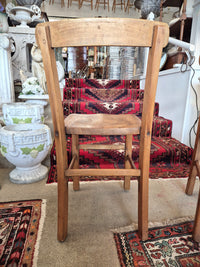 Wooden childs school chair on a patterned rug with decorative items in the background. back view.