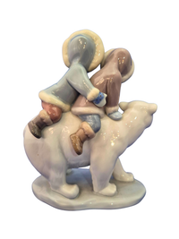 A ceramic figurine depicting two children riding a polar bear, shown against a plain white background.