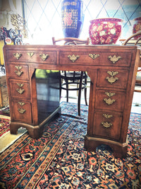 An antique wooden writing desk with ornate brass drawer pulls, set on a patterned oriental rug in a shop interior.