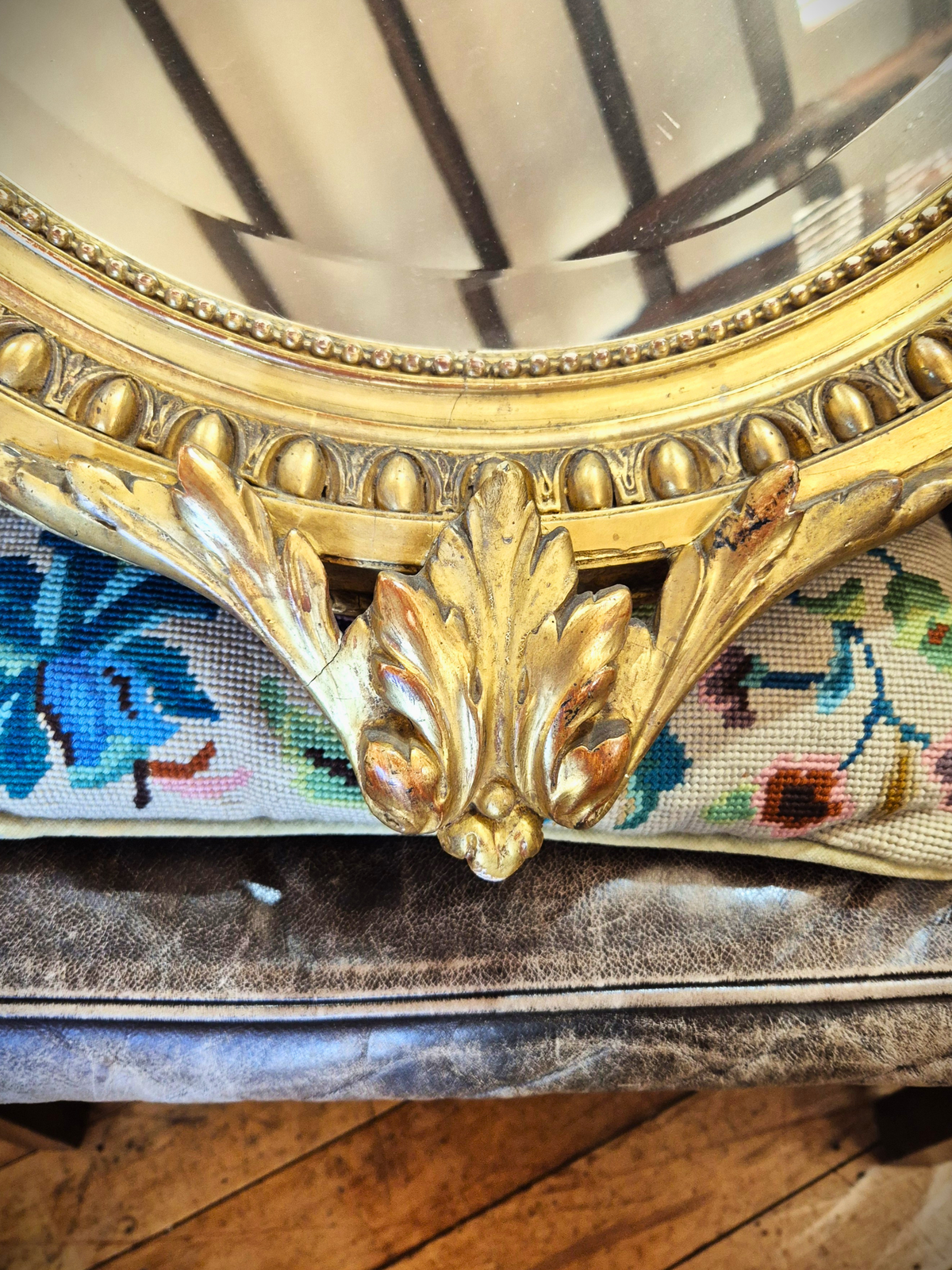 Close-up of a decorative gold mirror with intricate detailing on a wooden floor.