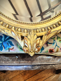 Close-up of a decorative gold mirror with intricate detailing on a wooden floor.